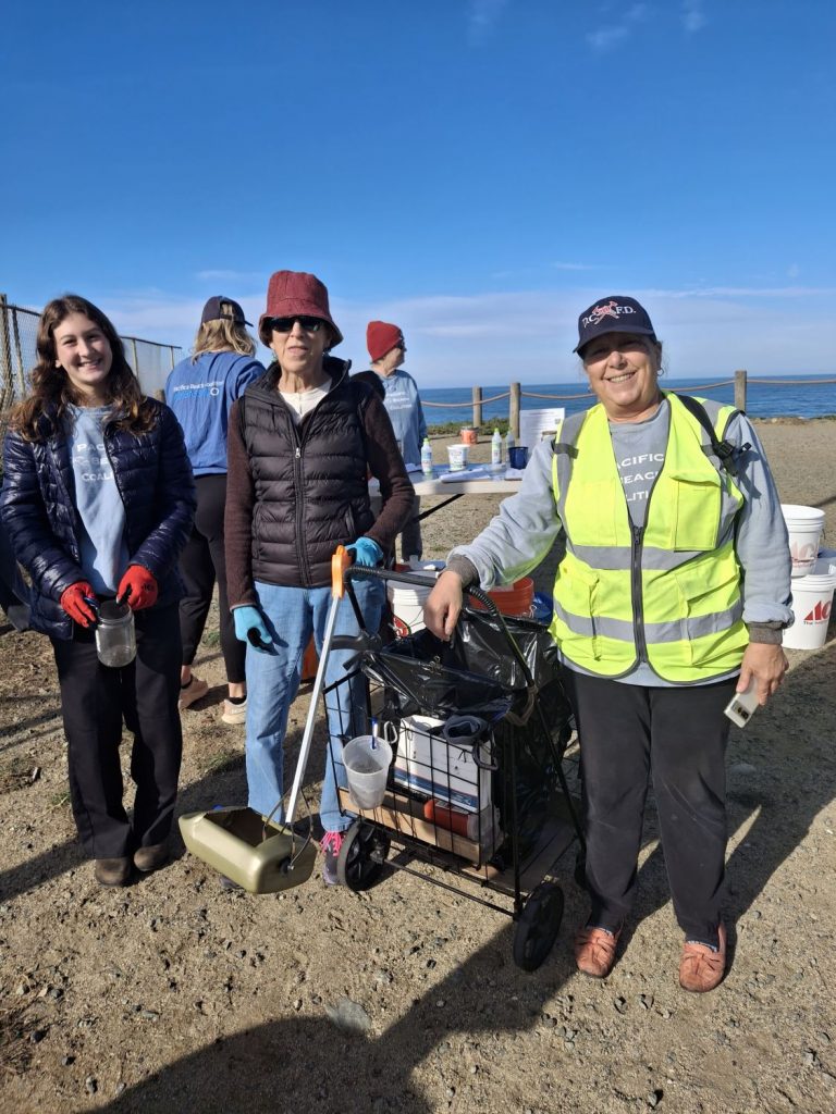 Three volunteers pick up trash at a beach cleanup