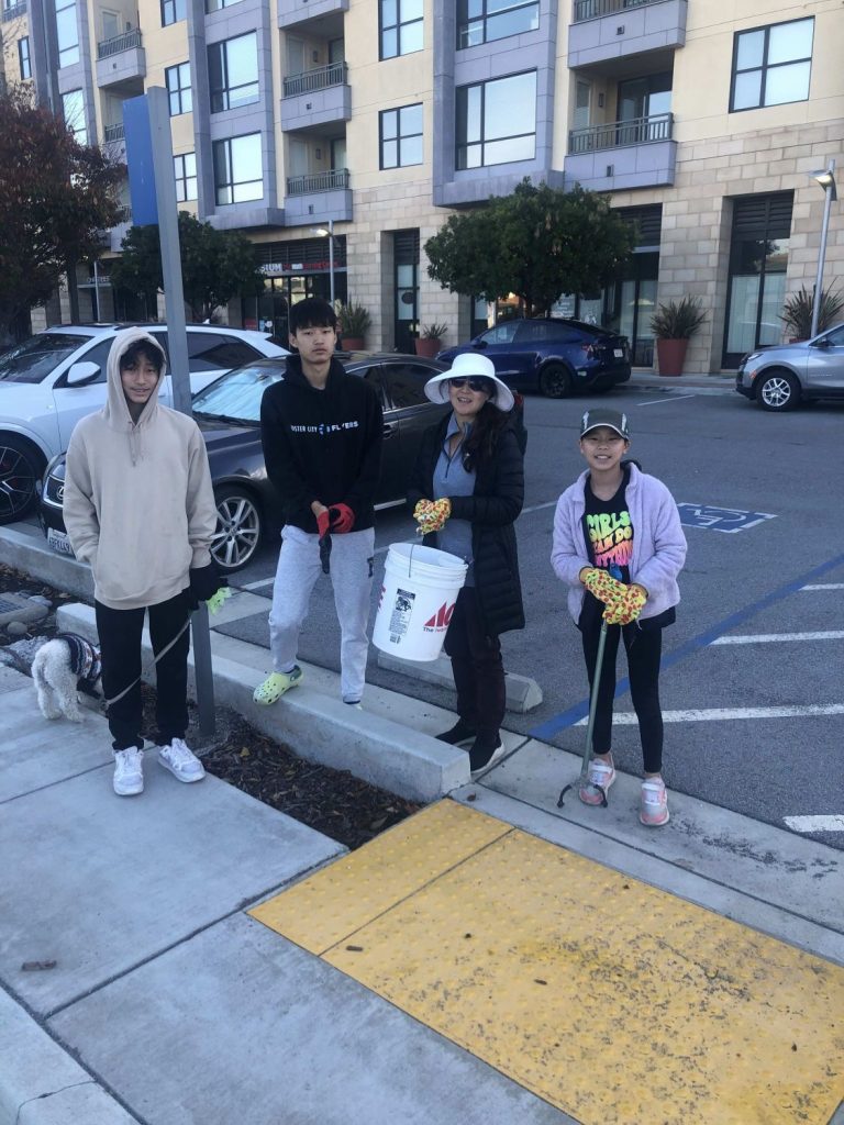 Four people stand on the sidewalk with trash pickers and buckets