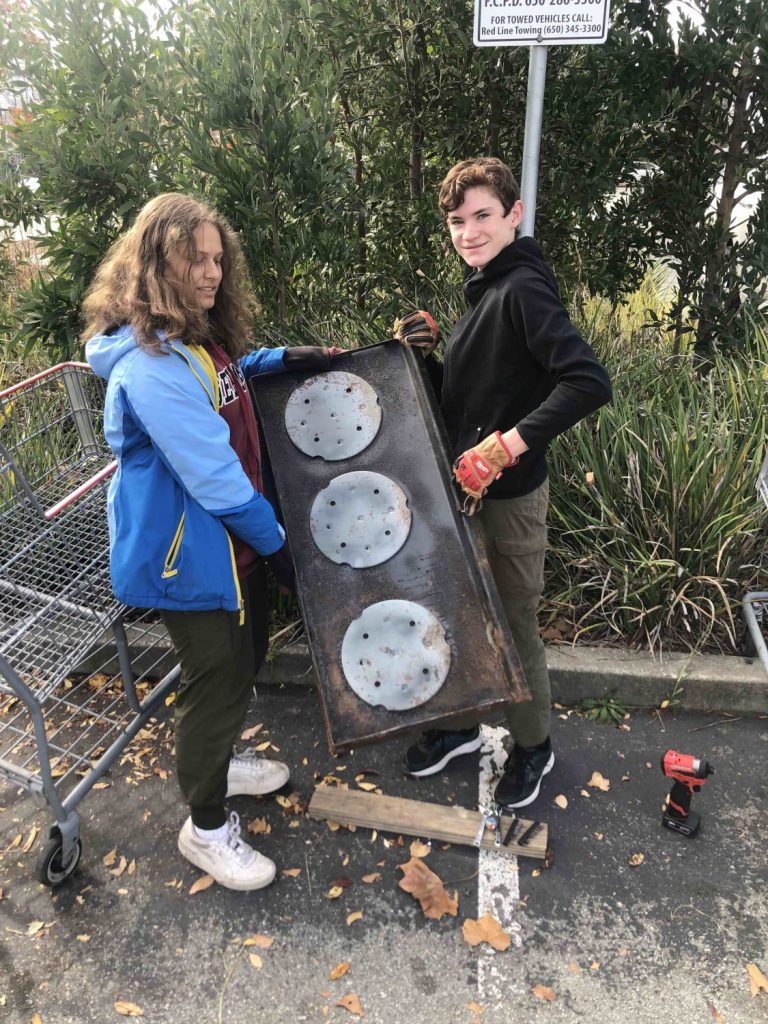 Two students hold a commercial cooking grill found at a community cleanup