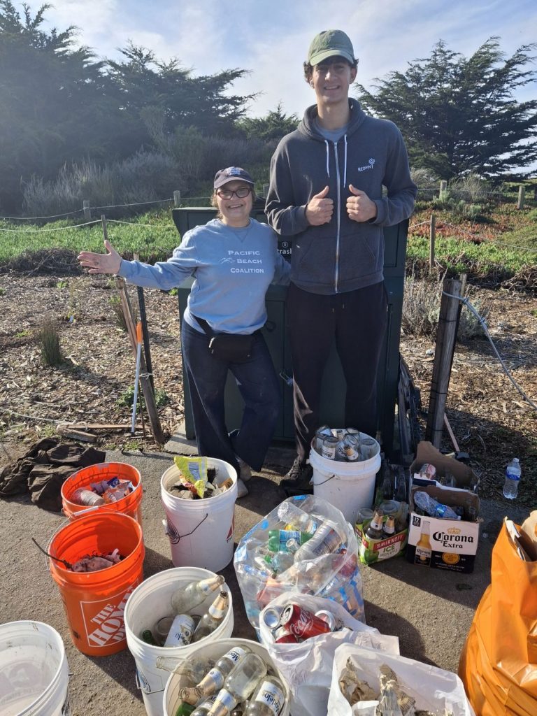 Two volunteers pose with buckets filled with recyclables picked up during a beach cleanup