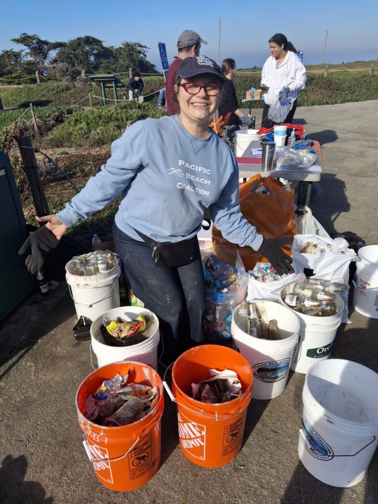 A female poses with buckets filled with recyclables and trash picked up during a beach cleanup