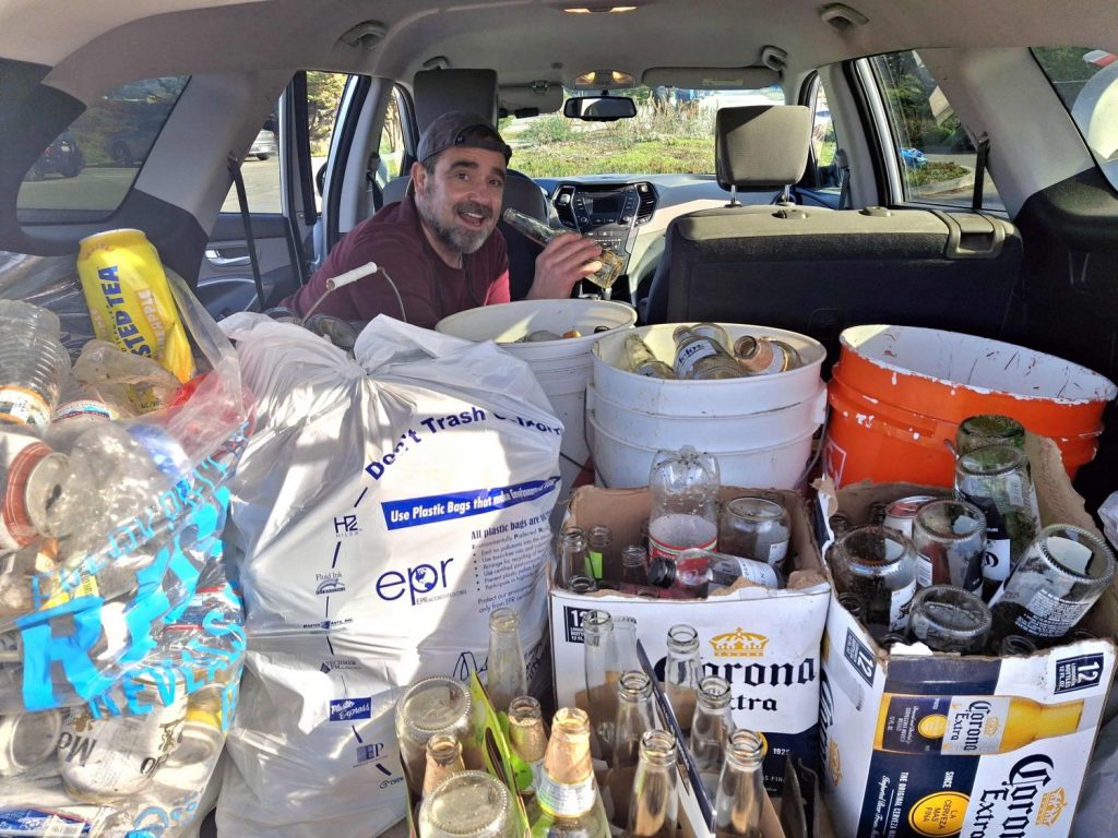 A male volunteer poses with 80 pounds of trashed beer bottles and cans in the trunk of an SUV