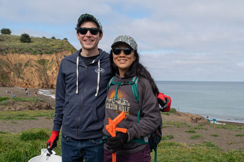 A couple poses with their beach cleanup supplies