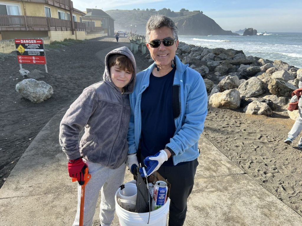 A child and adult pose with the trash they picked up at a beach cleanup