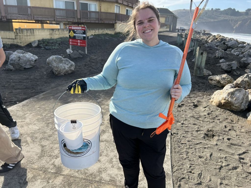 A female holds her bucket and trash picker at a beach cleanup