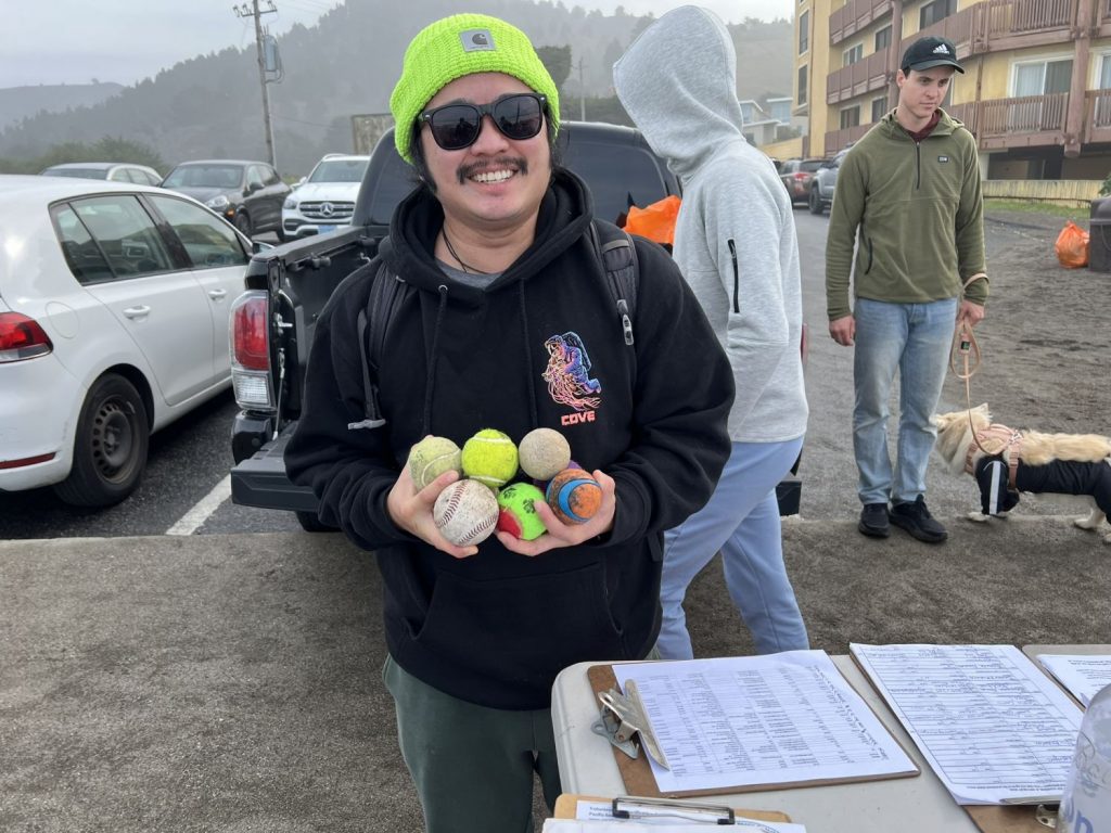 A smiling dog-walker poses with six tennis balls collected during beach cleanups