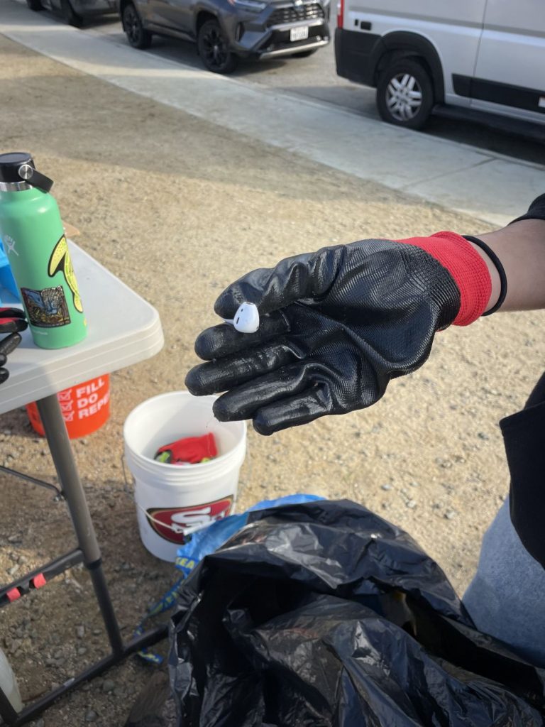 A volunteer finds an Apple AirPod at a PBC cleanup event