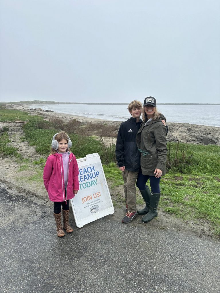 A family of three poses near the beach at a cleanup event