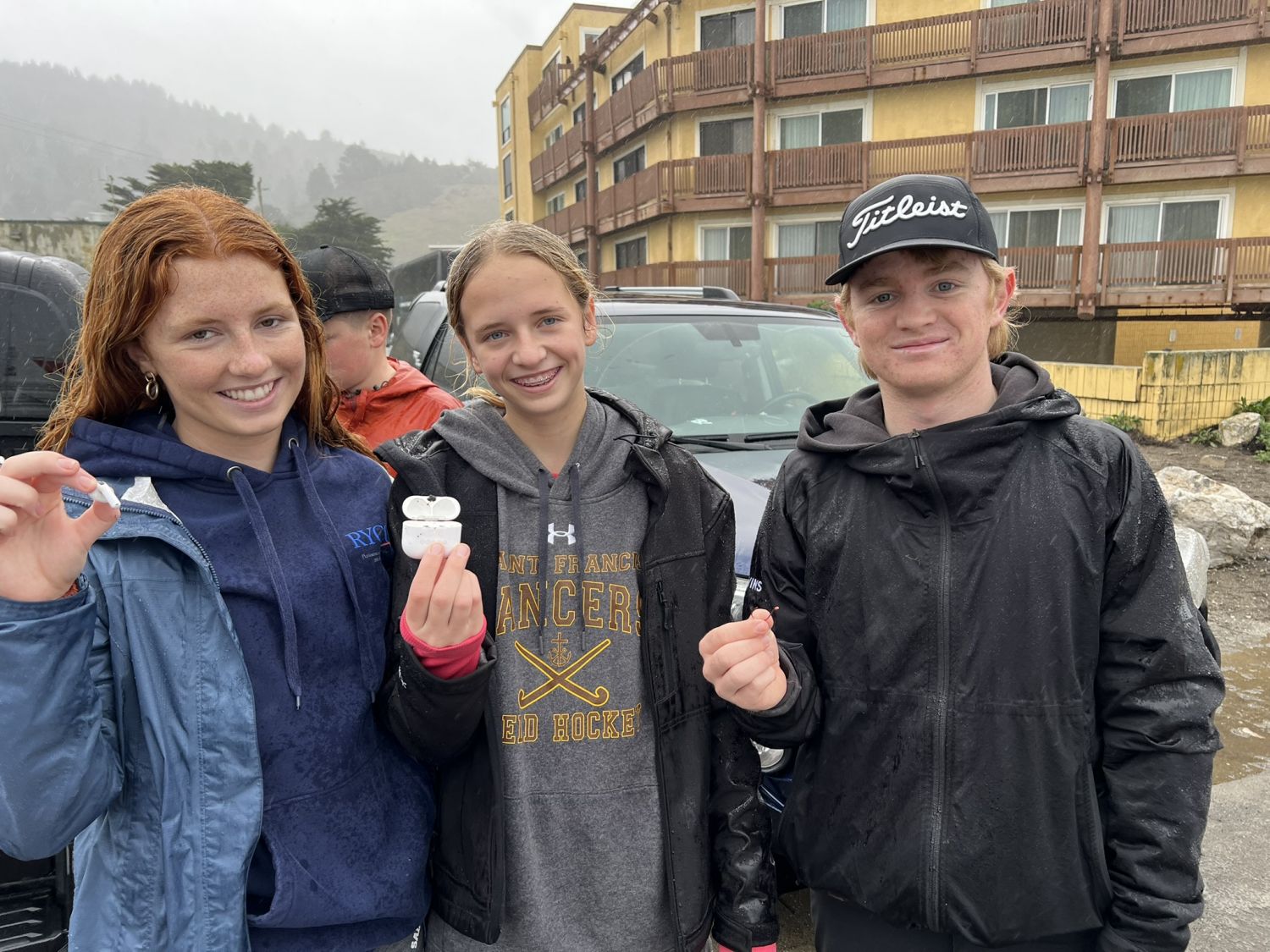 Three teen volunteers hold an Apple AirPod case and single AirPod at a February 2025 PBC cleanup